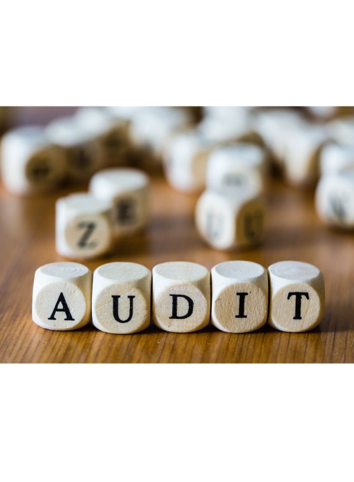  Five light-colored cubes on a wooden table, spelling out the word "Audit"