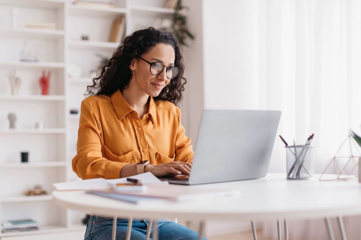 Middle Eastern Lady Using Laptop Working Online Wearing Eyewear Sitting At Workplace In Modern Offic